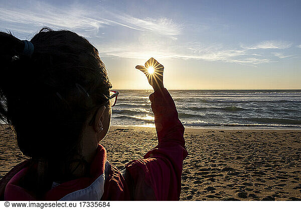 Frau hält Sonne am Strand bei Sonnenuntergang
