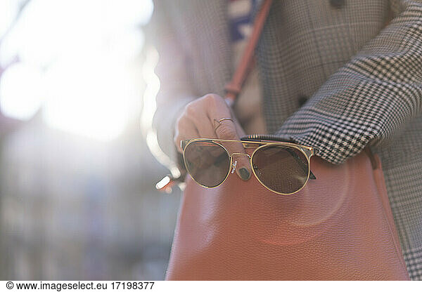 Frau hält Sonnenbrille  während sie in der Handtasche sucht