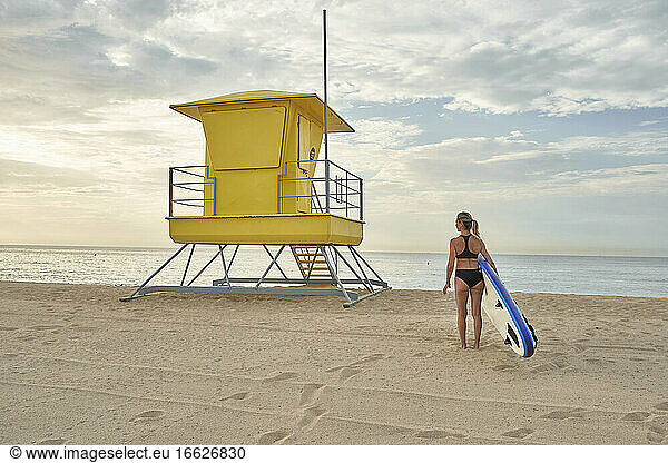 Frau hält Surfbrett am Strand während des Sonnenuntergangs