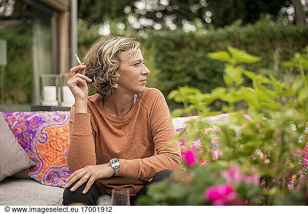 Frau hält Zigarette  während sie auf dem Sofa im Hinterhof sitzt