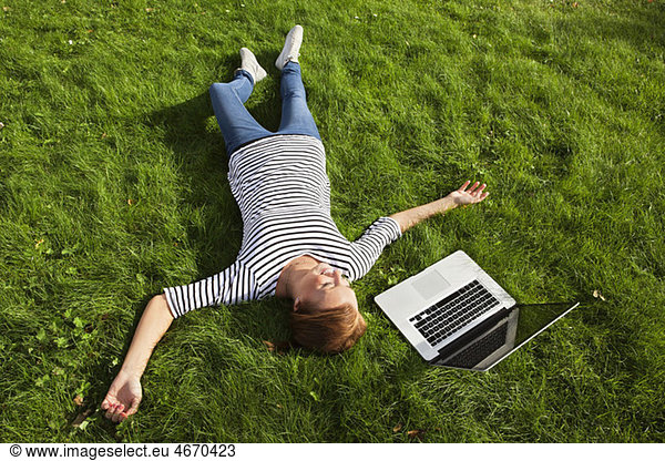 Frau im Gras neben dem Computer liegend