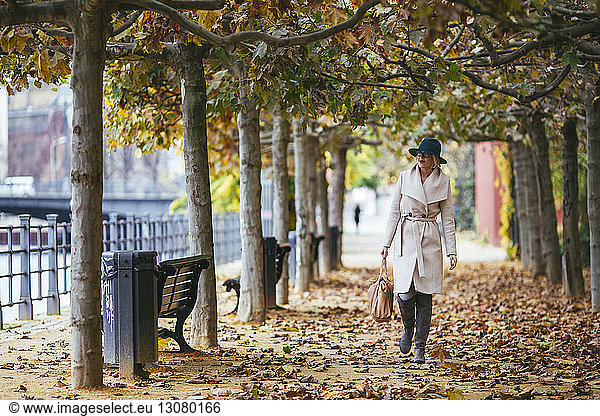 Frau im Mantel geht im Herbst auf einem Fußweg im Park