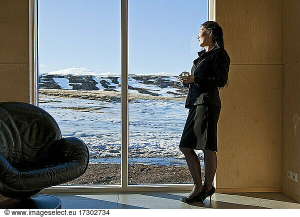 Frau in Business-Kleidung schaut aus dem Fenster eines Ferienhauses
