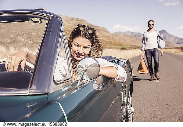 Frau in Cabriolet auf Autoreise und wartet auf Mann mit Reisetasche