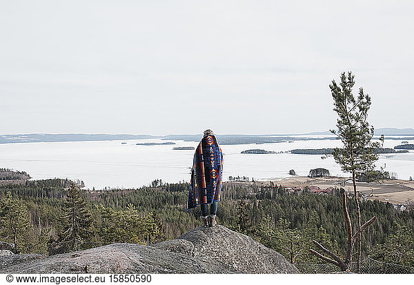 Frau in eine Decke gewickelt  die den Blick auf den Ozean und den Wald richtet