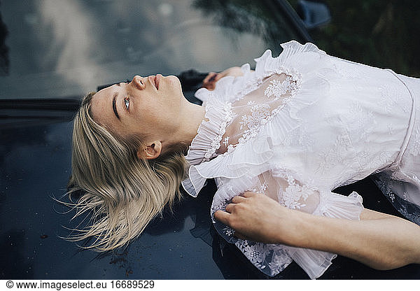 Frau in einem weißen Kleid auf der Motorhaube eines Autos liegend