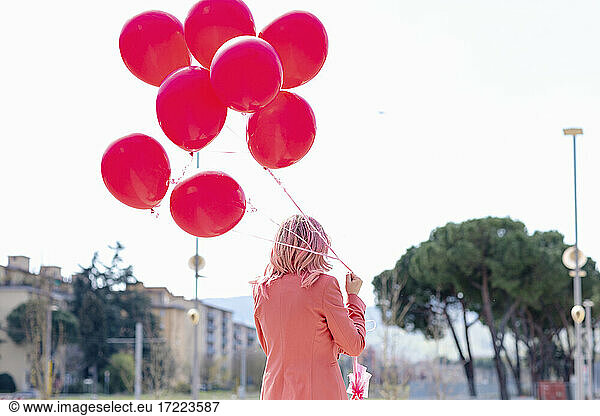Frau in eleganter Freizeitkleidung hält ein Bündel rosa Luftballons