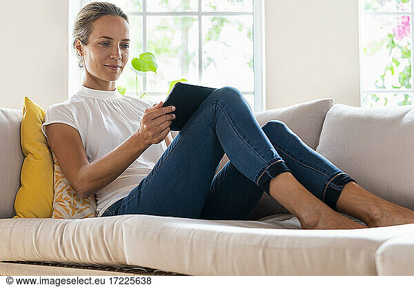 Frau in Freizeitkleidung schaut auf ein digitales Tablet auf dem Sofa