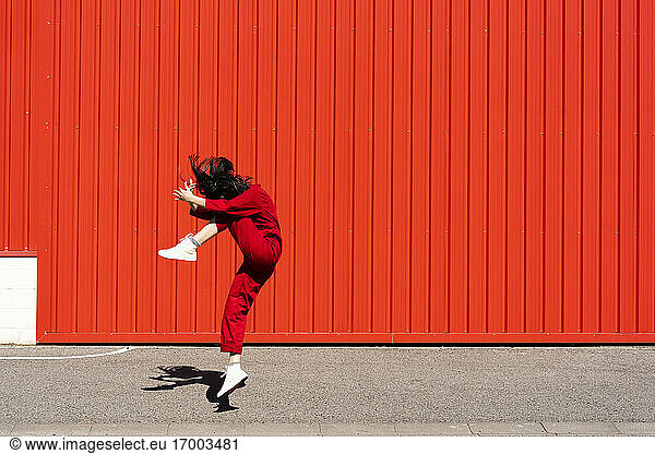 Frau in rotem Overall springt vor rotem Rolltor in die Luft