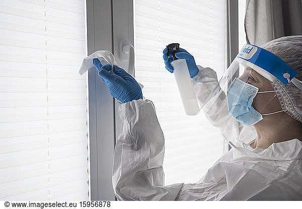 Frau in Schutzkleidung Desinfektionstuch am Fenster