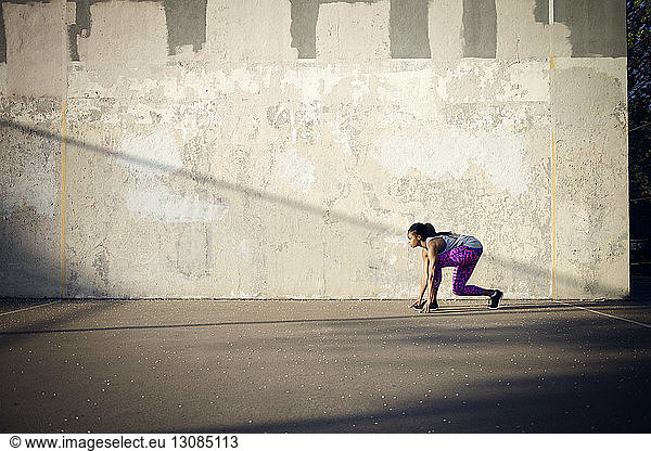 Frau in Startposition auf der Straße bereit  an der Mauer entlang zu laufen