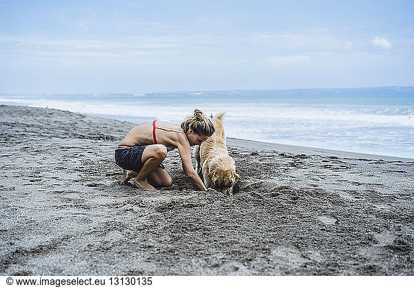 Frau in voller Länge und Labrador Retriever beim Graben am Ufer am Strand