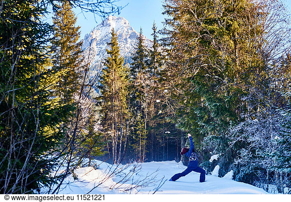 Frau in Winterkleidung praktiziert Krieger-Yoga-Pose im verschneiten Wald  Österreich