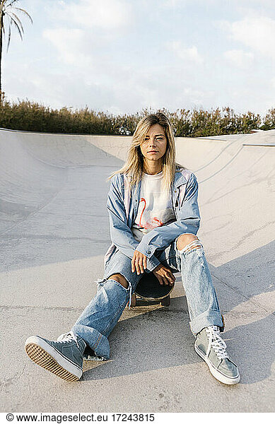 Frau in zerrissenen Jeans sitzt im Skateboard-Park