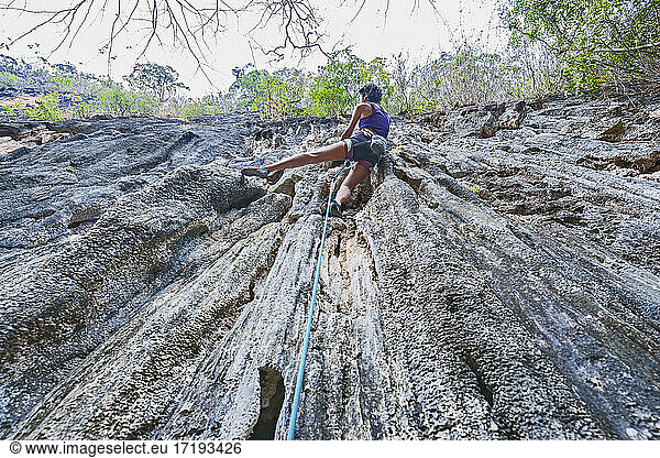 Frau klettert auf steilem Kalksteinfelsen in Laos