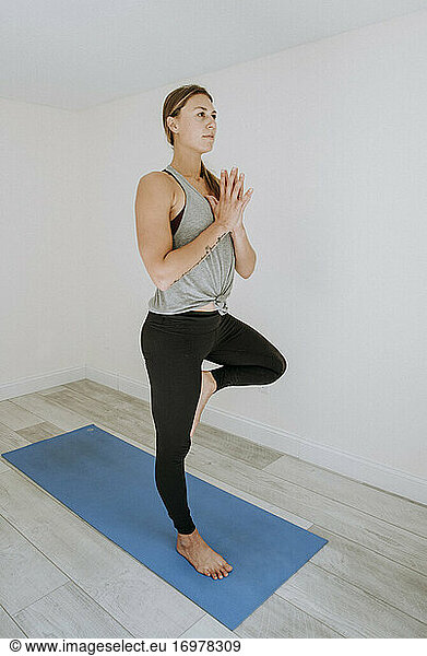 Frau konzentriert sich bei einer einfachen Yogapose im Haus auf einer blauen Matte