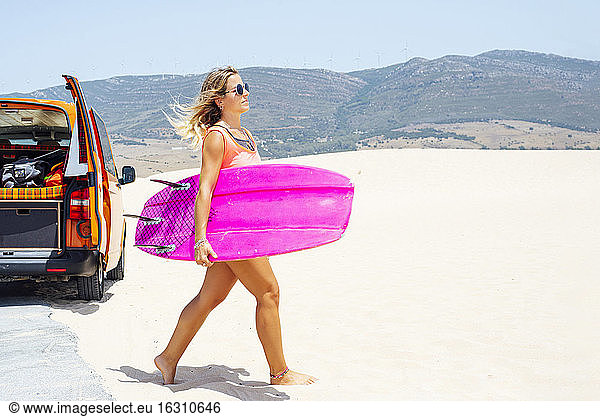 Frau läuft im Sand und hält ein Surfbrett am Strand an einem sonnigen Tag