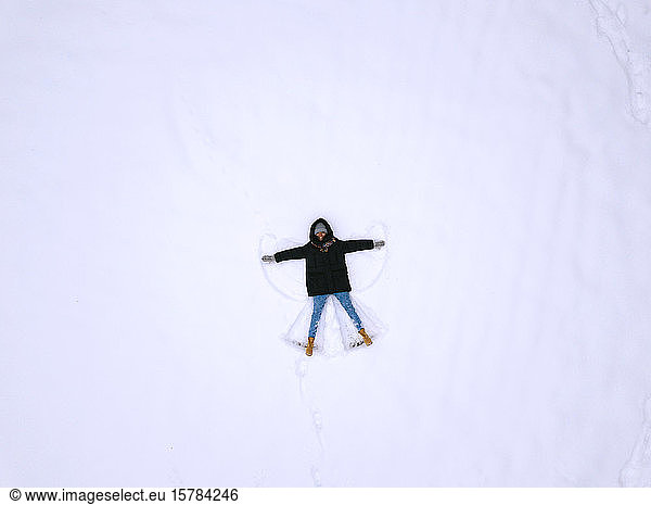 Frau liegt auf Schnee und macht Schnee-Engel