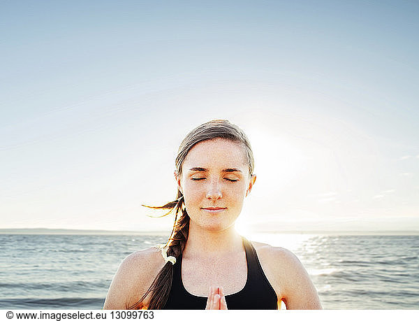 Frau meditiert in Lotus-Position am Meer gegen den Himmel