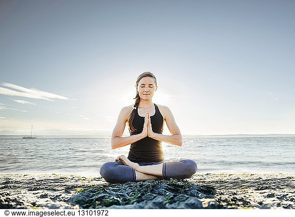 Frau meditiert in Lotus-Position am Strand gegen den Himmel