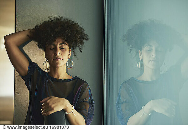 Frau mit Afro-Haar sitzt in einem Schaufenster. Sie hat die Augen geschlossen und die Hand im Haar.
