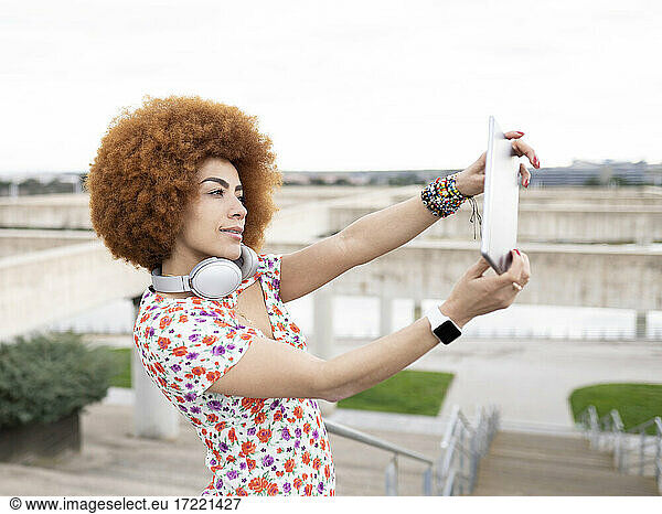 Frau mit Afrofrisur macht Selfie mit digitalem Tablet im Park