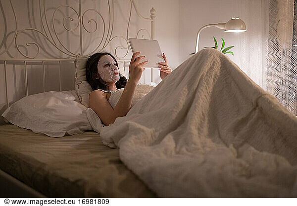 Frau mit Bettlakenmaske auf dem Bett liegend mit Tablette