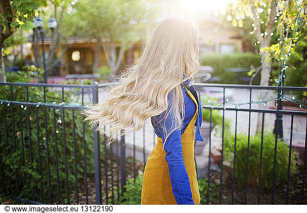 Frau mit blonden Haaren geht am sonnigen Tag am Park am Zaun vorbei