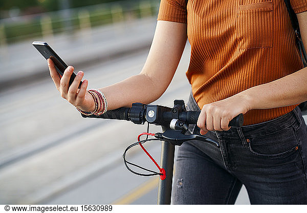 Frau mit Elektroroller mit Smartphone  Teilansicht