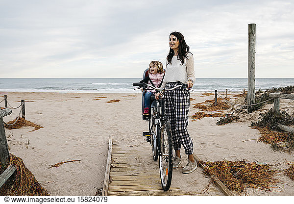 Frau mit Fahrrad auf einer Strandpromenade in den Dünen mit Tochter im Kindersitz