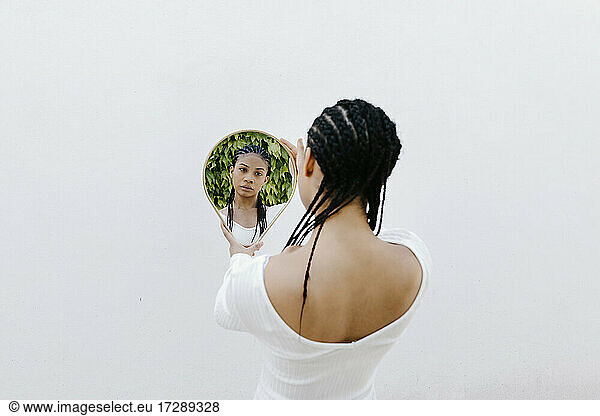 Frau mit geflochtenem Haar betrachtet ihr Spiegelbild im Spiegel