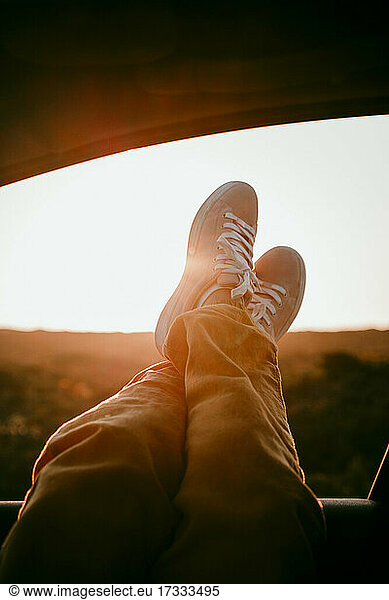 Frau mit gekreuzten Beinen am Autofenster bei Sonnenuntergang