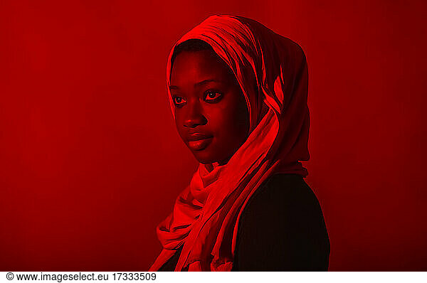 Frau mit Hidschab  die vor rotem Hintergrund wegschaut