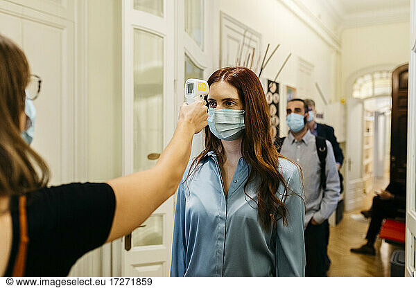 Frau mit Infrarot-Thermometer prüft die Temperatur einer Geschäftsfrau im Korridor