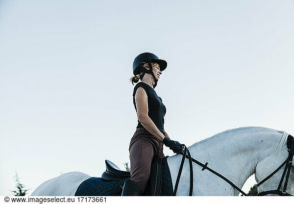Frau mit Kopfbedeckung reitet auf Pferd gegen klaren Himmel