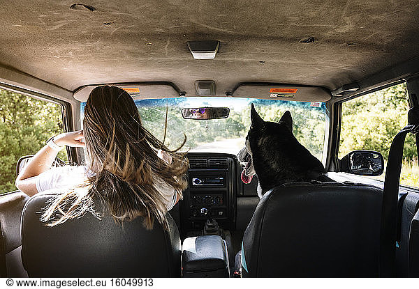 Frau mit langen blonden Haaren fährt mit Husky auf Road Trip