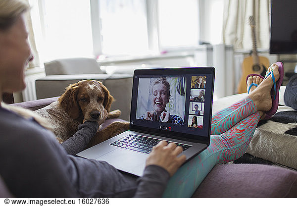 Frau mit Laptop im Video-Chat mit Freunden auf dem Sofa mit Hund