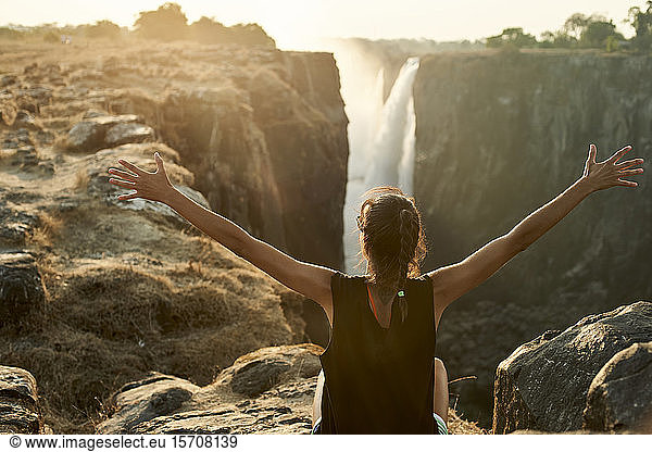 Frau mit offenen Armen genießt den Blick auf die Victoriafälle  Simbabwe