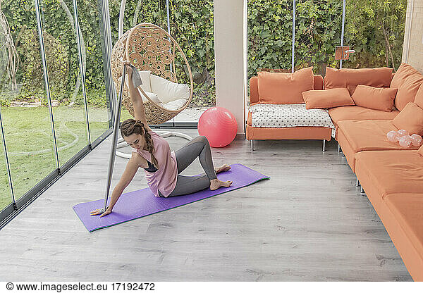 Frau mit Pferdeschwanz in Yoga-Position mit Stretching-Band  Home Fitness
