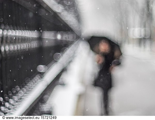 Frau mit Regenschirm geht entlang eines Gitters  Schneefall  unscharf  Wien  Österreich  Europa