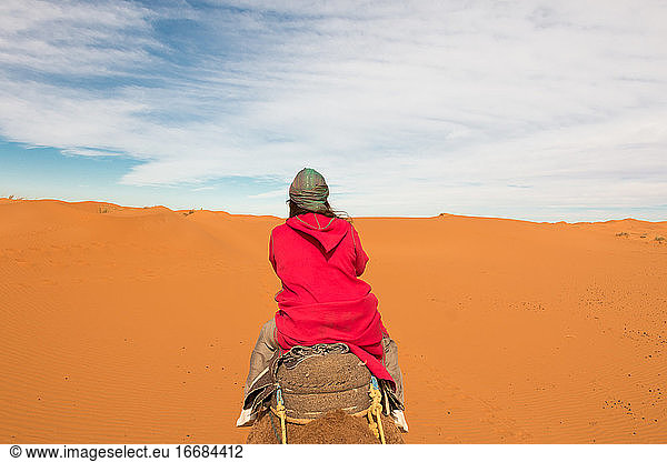 Frau mit rosa Djellaba reitet auf einem Kamel in den Dünen der Wüste