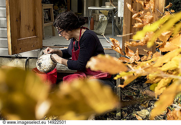 Frau mit roter Schürze sitzt vor ihrer Keramikwerkstatt und hält eine Vase.