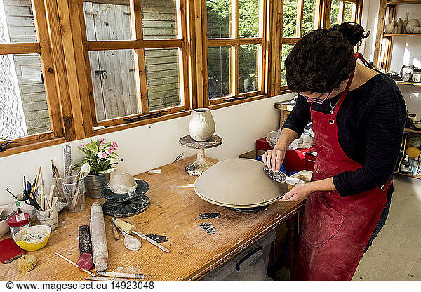 Frau mit roter Schürze steht in ihrer Keramikwerkstatt und arbeitet an einer Tonschüssel.