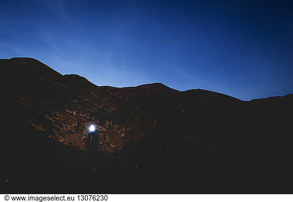 Frau mit Scheinwerfer steht am Berg vor blauem Himmel