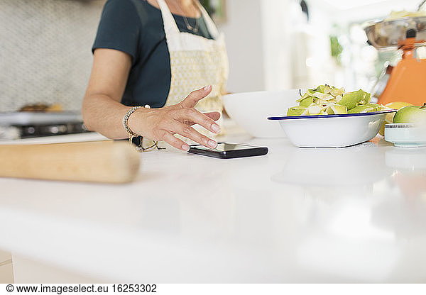 Frau mit Smartphone backt an der Küchentheke