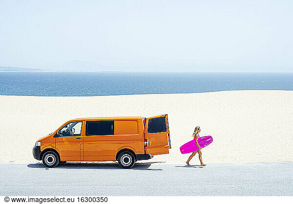 Frau mit Surfbrett am Strand an einem sonnigen Tag