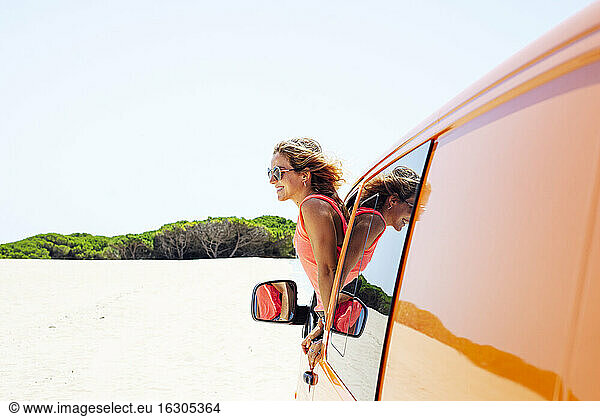 Frau mit wehendem Haar lehnt sich durch das Fenster aus dem Auto