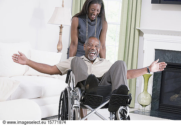 Frau mittleren Alters  die einen Mann mittleren Alters  der in einem Rollstuhl sitzt  lächelnd nach unten schiebt