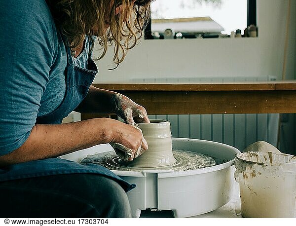 Frau modelliert Ton auf einer Töpferscheibe in einem Atelier im Vereinigten Königreich