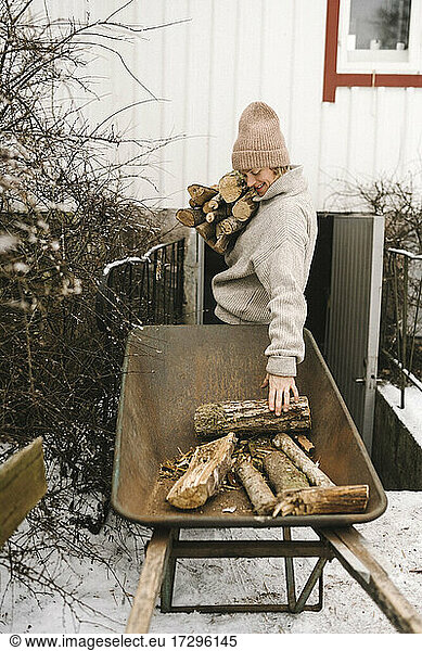 Frau sammelt Brennholz aus Schubkarre im Winter